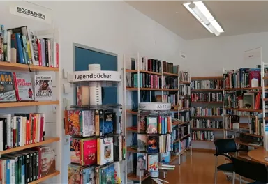 A modern room with shelves full of books in a library. There is a reading table and a cozy atmosphere.