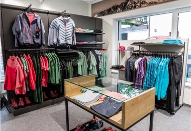 A modern retail space featuring sports clothing. Shelves are filled with colorful jackets and T-shirts, while a table with additional items stands in the middle.