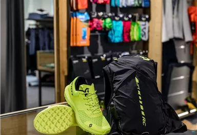A pair of bright yellow sports shoes is lying next to a black backpack in a sports store. In the background, various sportswear in colorful colors can be seen.