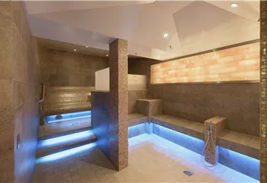A modern spa with soft lighting effects. The walls are made of stone and there are comfortable seating areas for relaxation.
