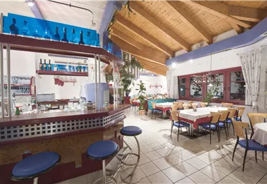 An inviting restaurant with a modern bar area and tables. The wooden ceiling and plants create a warm atmosphere.