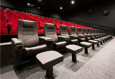 Ein modernes Kino mit bequemen, schwarzen Sitzen und roten Plätzen. Der Raum ist dunkel und einladend, ideal für ein Filmvergnügen.