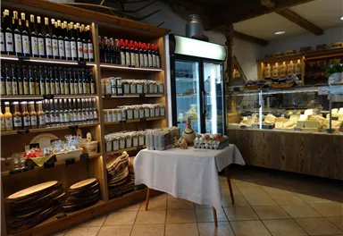 A cozy shop with shelves full of wine and vinegars. On a table are cheeses and various delicacies.