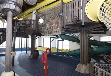 An indoor playground with slides and a climbing area. The colorful structures and bright light create a friendly atmosphere for children.