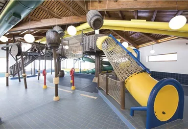 A play area with climbing frames and slides in a bright room. The equipment consists of colorful elements, ideal for children.