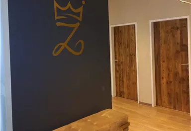 A modern entrance area with a decorative wall and a stylized crown. On the right, there are two wooden doors, and a padded bench stands in front of them.