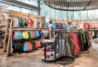 Ein farbenfroher Sportbekleidungsraum mit verschiedenen Kleidungsstücken und Zubehör. Die Ware ist ordentlich auf Regalen und Ständern platziert.