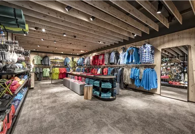 Ein Sportbekleidungsgeschäft mit einer Vielzahl von Kleidung in lebhaften Farben. Regale sind ordentlich angeordnet, und ein großer Spiegel ist sichtbar.