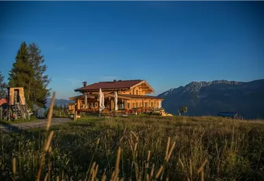 A rustic wooden house in a picturesque mountain landscape. Surrounded by meadows and mountains under a clear blue sky.