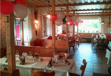 Ein gemütliches Restaurant mit festlich dekorierten Tischen. Rote, weiße und schwarze Luftballons schmücken den Raum.