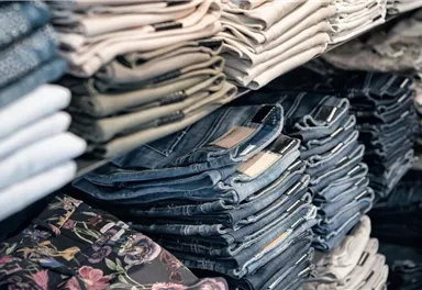 Eine große Auswahl an zusammengefalteten Jeans in verschiedenen Farben und Mustern. Die Hosen sind ordentlich gestapelt und gut organisiert.