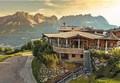 A picturesque building on a hill overlooking majestic mountains. The evening sun bathes the landscape in warm light.