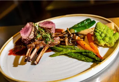 A stylish dish with lamb chops and colorful vegetables. The food is attractively presented and includes fresh herbs.