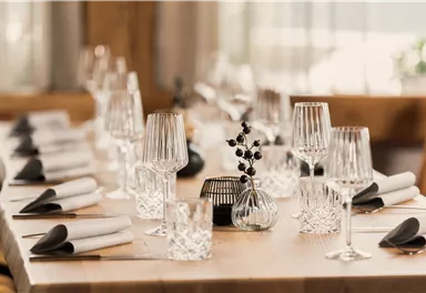 An elegantly set table with glasses and napkins. In the center is a small flower vase that lightens the ambiance.