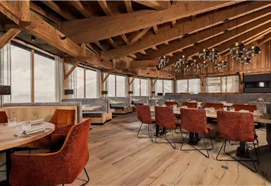 A modernly furnished restaurant with wooden walls and large windows. Red chairs and stylish lamps create an inviting atmosphere.