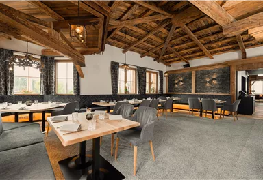 A cozy restaurant with a wooden ceiling and modern furniture. The tables are elegantly set, and the windows offer a lovely view.