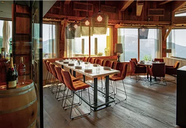 A cozy restaurant with a long table and modern chairs.
Large windows offer a view of the mountains and let in a lot of light.