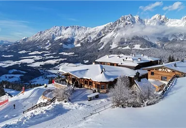 A picturesque alpine landscape with snow-covered mountains and a log cabin. The clear blue sky adds a serene atmosphere.