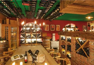 A cozy wine cellar with shelves full of wine bottles. A long table and candles create an inviting atmosphere.