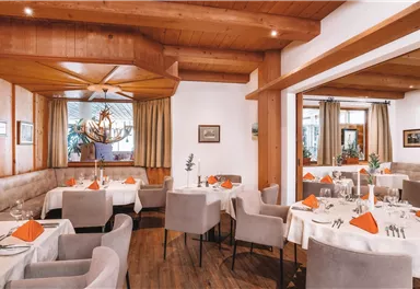 An elegant restaurant with warm wooden decor and cozy tables. The tables are neatly set and decorated with orange napkins.