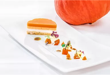 An artistically arranged dessert with a layer of pumpkin and a crunchy base. Next to it is a fresh pumpkin.