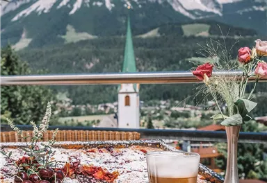 A beautiful view of the mountains with a set table. In the foreground, there is a glass of beer and a plate of delicious food.