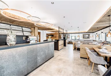 Ein modernes Restaurant mit hellen Holzelementen und eleganten Beleuchtung. Der Empfangsbereich ist offen und einladend, mit stilvollen Tischen und Stühlen.