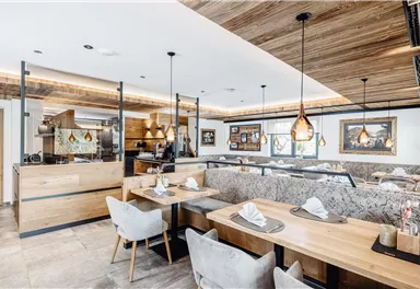 Ein modernes Restaurant mit Holzdekor und elegantem Design. Es gibt stilvolle Tische und eine offene Küche im Hintergrund.