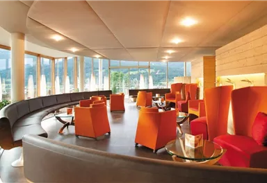 A modern and stylish lounge with large windows and an inviting atmosphere. The decor consists of elegant orange chairs and tables.