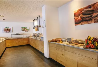 A bright buffet with wooden materials and a selection of fresh fruits. In the background, appealing images of dishes can be seen.