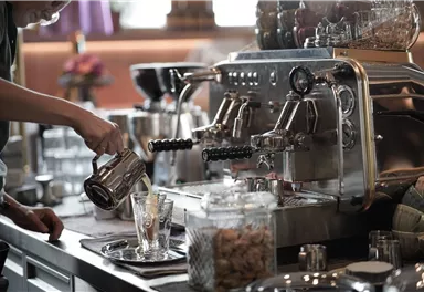 A modern espresso machine in a café. Someone is pouring coffee into a glass.