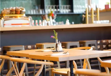 A cozy café with wooden tables and chairs. On the table, there is a small vase with a flower.