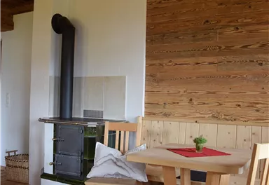 Ein gemütlicher Raum mit Holzverkleidung und Möbeln. Ein Ofen steht neben dem Tisch und Stühlen.