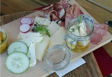 Ein hübsches Brett mit Wurst, Käse und frischem Gemüse. Dazu gibt es ein Glas mit Kräuterbutter.