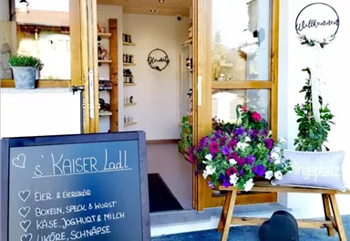 An inviting shop entrance with wooden doors and colorful flowers. In the foreground, there is a sign offering fresh produce and gifts.