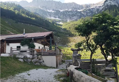 A cozy cabin in the middle of a picturesque mountain landscape. In the background, green meadows and high mountains can be seen.