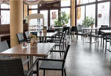 A modern restaurant with many tables and chairs. Large windows let in a lot of light, and there are plants distributed around the rooms.