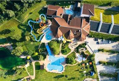 A large recreational facility with several swimming pools and slides. The complex is surrounded by green meadows and trees.