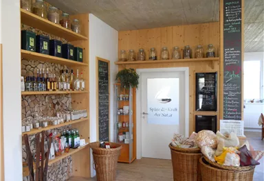An inviting shop with shelves full of herbs and ingredients. On the wall are price boards and decorative baskets with natural products.