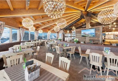 A cozy restaurant with wooden decor and large windows. Bright chandeliers create an inviting atmosphere.