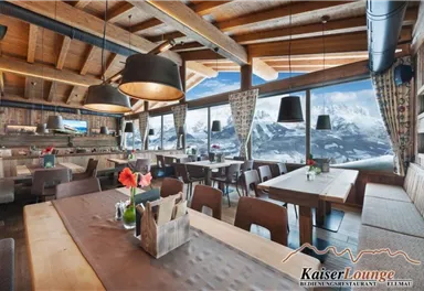 A cozy restaurant with wooden decor and modern lamps. Large windows offer a view of the mountains and let in plenty of daylight.