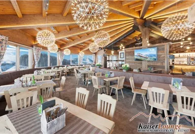 Ein modernes Restaurant mit holzverkleideten Wänden und großen Fenstern. Der Raum ist hell und einladend, mit stilvollen Kronleuchtern und gemütlichen Tischen.
