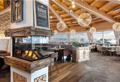 Ein stilvolles Restaurant mit gemütlicher Atmosphäre und großen Fenstern, die einen Blick auf die Berge bieten. Der Kamin aus Holz sorgt für eine einladende Stimmung.