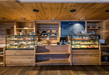 A cozy café with wooden furniture and glass display cases. The display cases showcase a selection of freshly baked pastries and snacks.