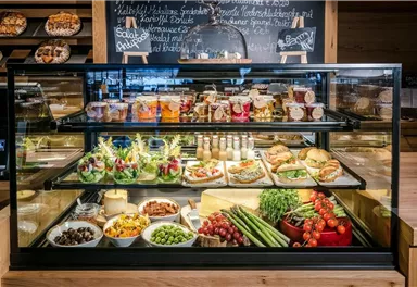 An appealing display case with various delicious dishes and snacks. On the table, salads, sandwiches, and fresh fruit are visible.