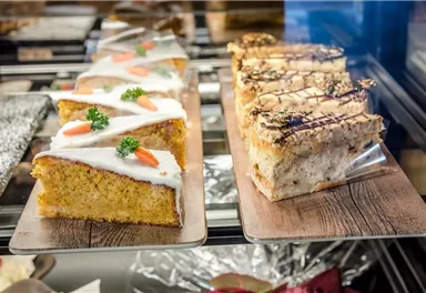 A selection of delicious cakes in a display case. On the left, a carrot-shaped cake with frosting and decoration, on the right, a sleek cake with chocolate and nuts.