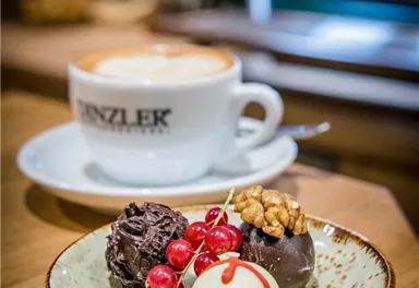 A cup of coffee is next to a plate with three delicious pralines and red currants. The atmosphere is cozy and inviting.