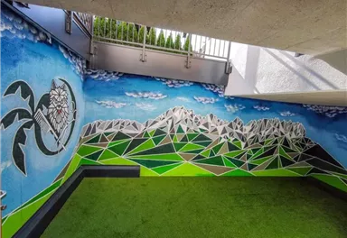 A colorful mural featuring a mountain panorama and blue sky. The ground is covered with green artificial turf.