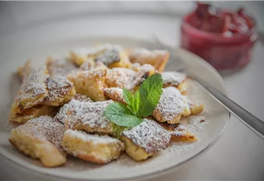A plate with delicious Kaiserschmarrn, sprinkled with powdered sugar and a fresh mint leaf. Next to it, a glass with red fruit sauce.