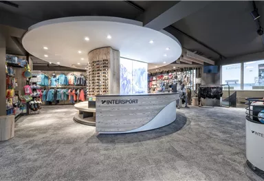 Ein modernes Sportgeschäft mit einem runden Empfangstresen und gut sortierten Regalen. Die Wände sind mit Sportbekleidung und Ausrüstung in verschiedenen Farben und Größen dekoriert.